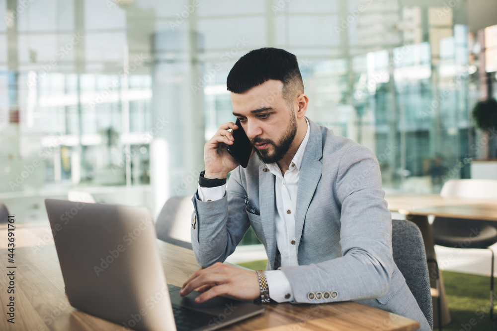 Busy male entrepreneur talking on smartphone and browsing laptop