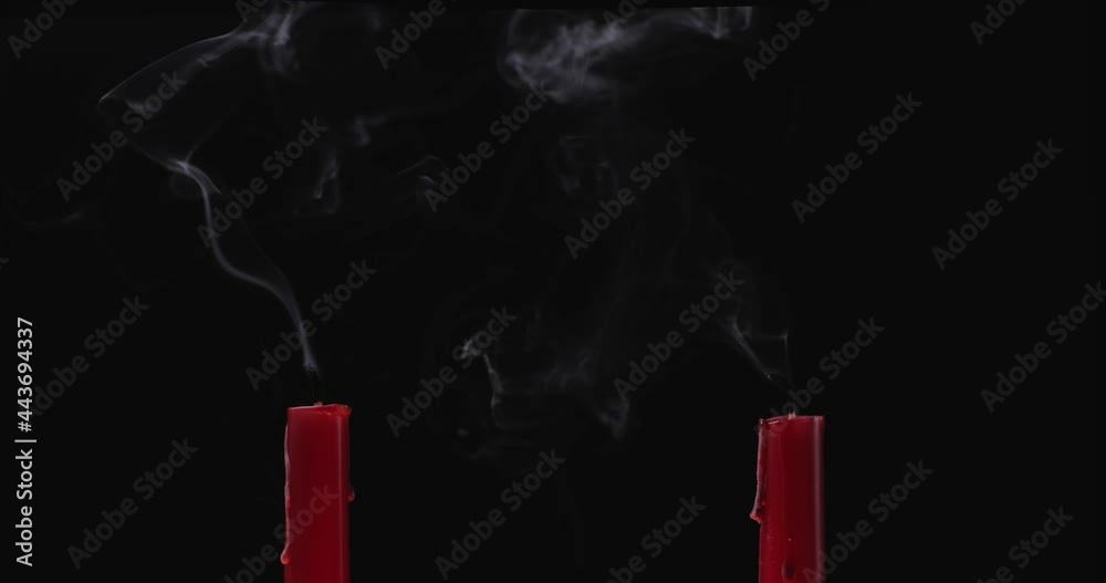 Two red candles are lit on a black background. A gust of wind suddenly