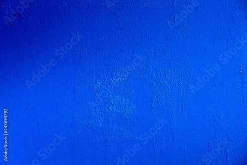 An old metal wall painted with a new blue paint similar to the color of the sea. There is uneven illumination of the surface. The texture of the previous layers of paint and glue comes in. Background. © Анатолий Еремин
