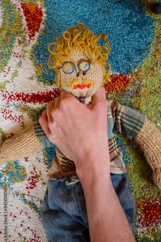 Eine männliche Strickpuppe wird von einer Hand gewürgt und festgehalten. Dem Typ geht es an den Kragen. Gewalt von Frauen an Männern. Voodoopuppe eines stereotypen Ingenieurs. Erwürgen und Erdrosseln  photo