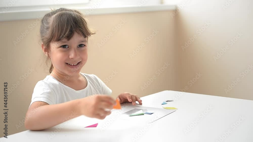 A preschooler girl sitting at the table collects a drawing from a geometric figure. the concept of early childhood development by montessori. a game of logic and imagination. A preschooler girl sitting at the table collects a drawing from a geometric figure. the concept of early childhood development by montessori. a game of logic and imagination.