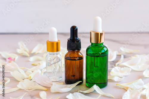 Face serum in a glass bottles with a pipette, poeny petals on marble background. Blank label package for branding mock-up. Spring cosmetics concept. Natural organic beauty product.