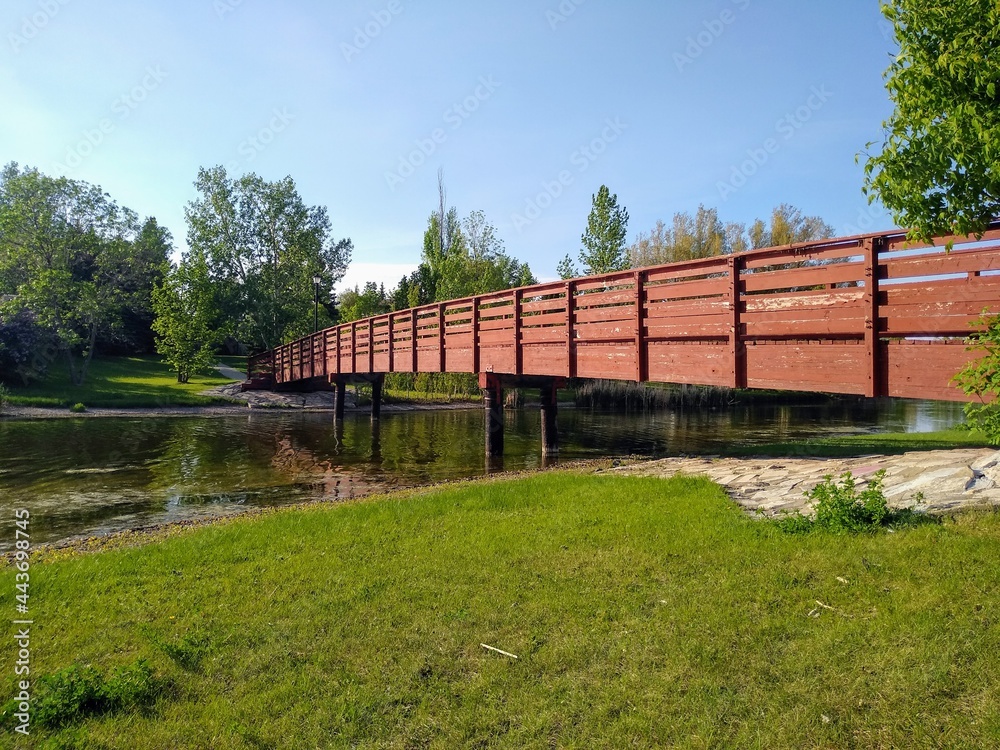 Panoramic view of a wooden, brown bridge with railings across the river.
