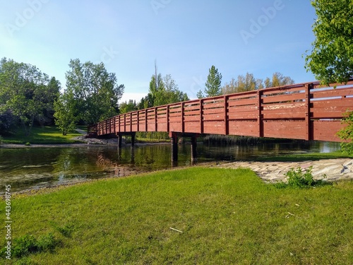 Panoramic view of a wooden, brown bridge with railings across the river. © Ilya Gromak
