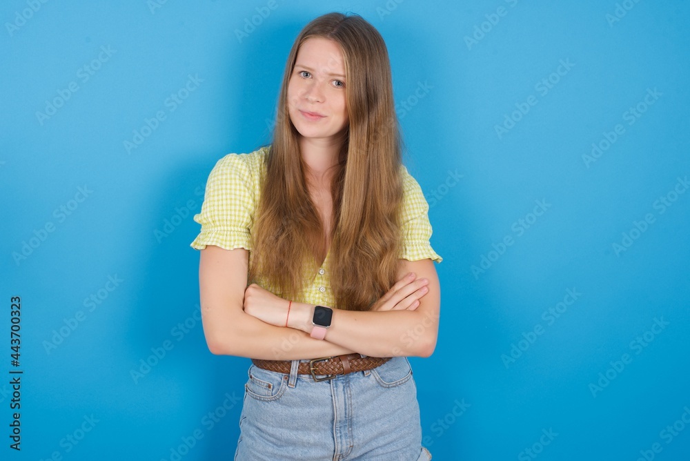 Waist up shot of self confident young beautiful blonde woman standing against blue background has broad smile, crosses arms, happy to meet with colleagues. Waist up shot of self confident young beautiful blonde woman standing against blue background has broad smile, crosses arms, happy to meet with colleagues.