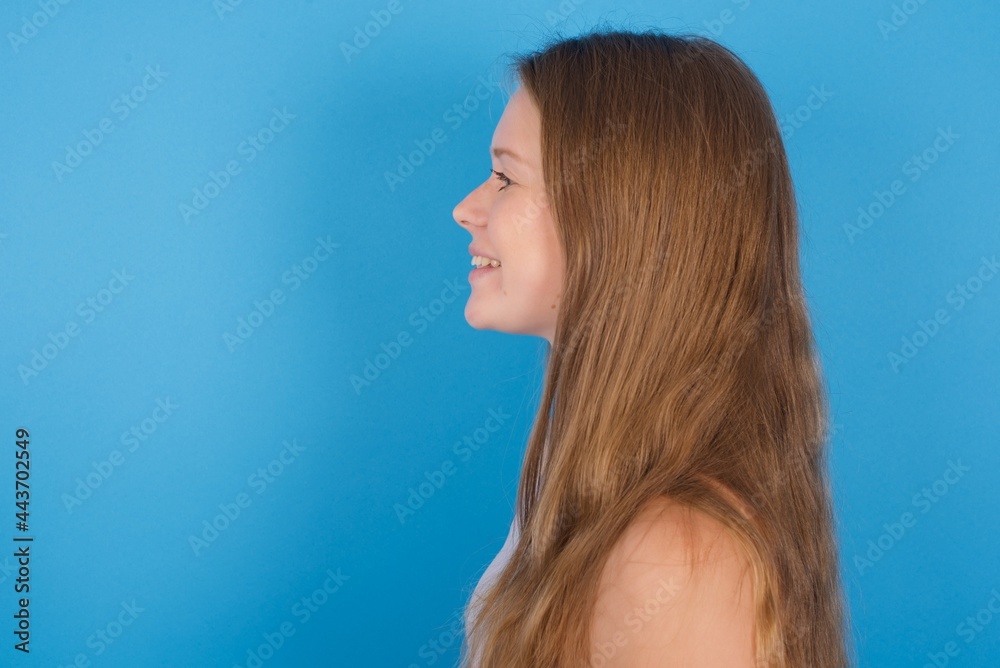 Profile portrait of nice young beautiful blonde woman standing against blue background look empty space toothy smile Profile portrait of nice young beautiful blonde woman standing against blue background look empty space toothy smile