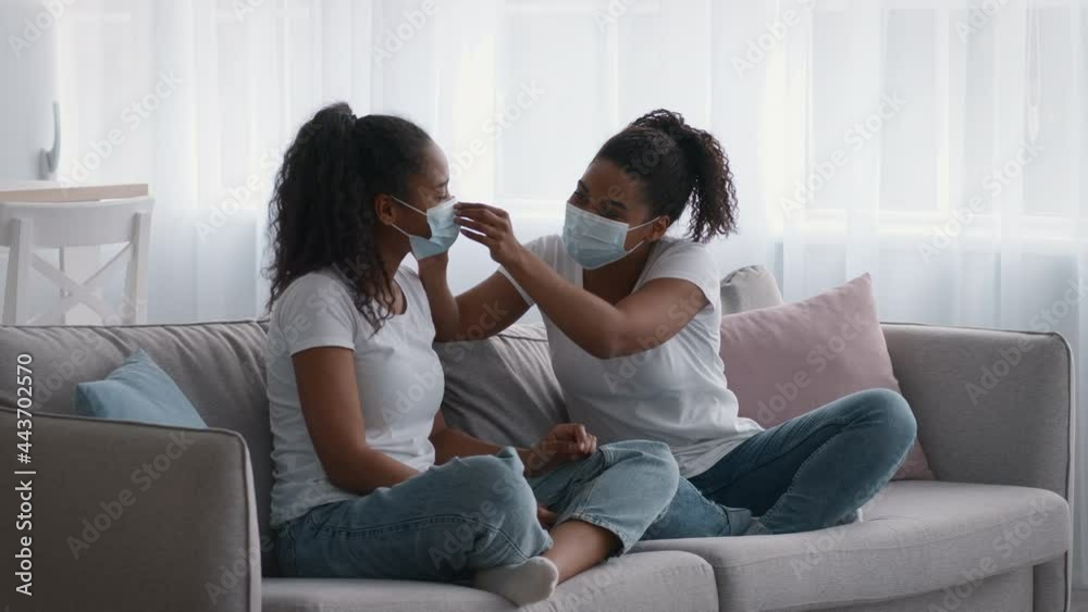 African american mother with her teen daughter putting on protective medical masks before going out, woman helping girl African american mother with her teen daughter putting on protective medical masks before going out, woman helping girl