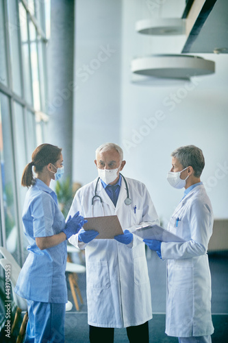Team of doctors wearing face masks while communicating in hallway at medical clinic.