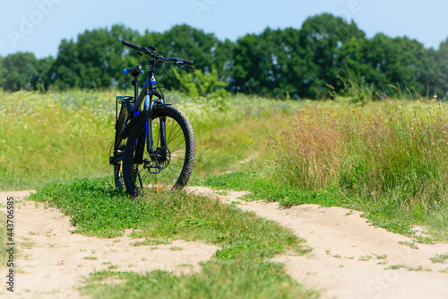 bike stands on the road in the field. A mountain bike stands on a field path with green grass. Mountain bike, blooming summer field, meadow flowers, sunny day. ride a bike. outdoor activities