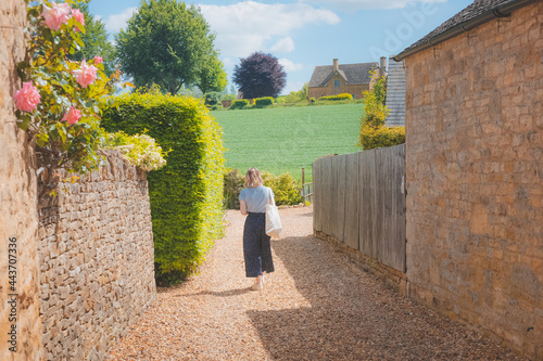 A young blonde female tourist explores a quaint country lane in the rural English countryside village of Chipping Campde, on a summer day in the Cotswolds, Gloucestershire, UK. photo