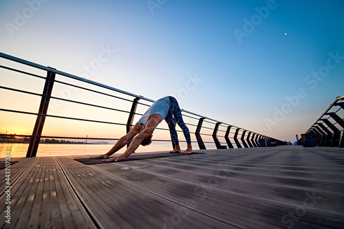 Man practicing yoga at sunset and doing dog face down