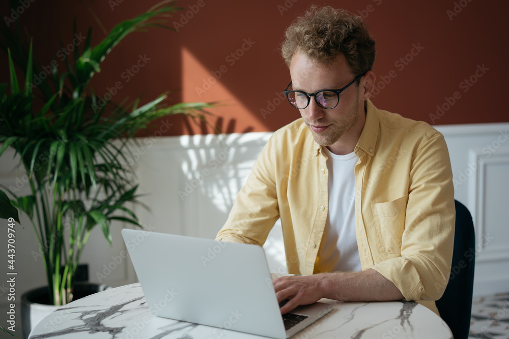 Successful freelancer copywriter working from home. Pensive man using laptop computer typing on keyboard, watching online training courses. Portrait of young handsome programmer sitting at workplace Successful freelancer copywriter working from home. Pensive man using laptop computer typing on keyboard, watching online training courses. Portrait of young handsome programmer sitting at workplace