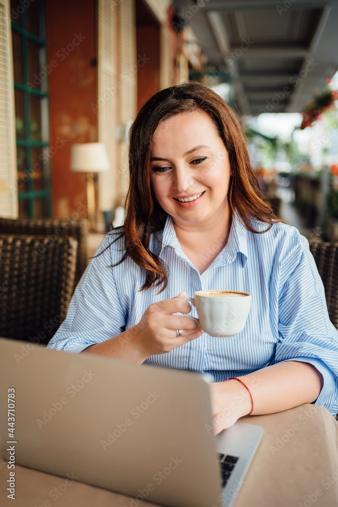 happy woman sits with laptop in cafe on street and drinks coffee happy woman sits with laptop in cafe on street and drinks coffee