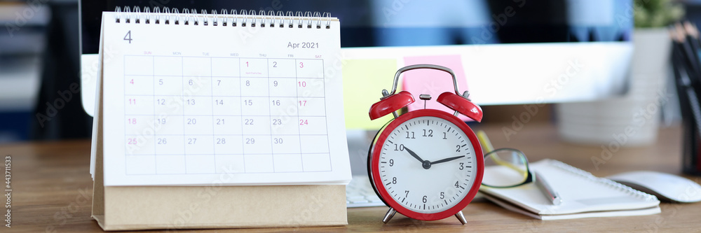 Calendar for April 2021 is on desktop next to alarm clock Calendar for April 2021 is on desktop next to alarm clock