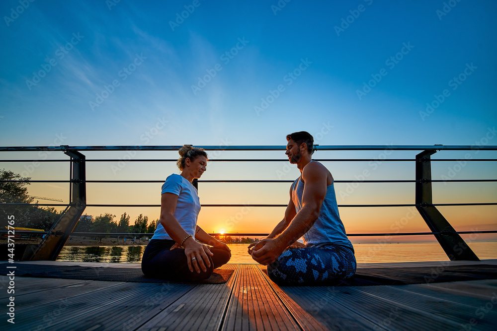 Fit young couple doing yoga, lotus pose. Healthy lifestyle. People outdoor sport activity on family vacation