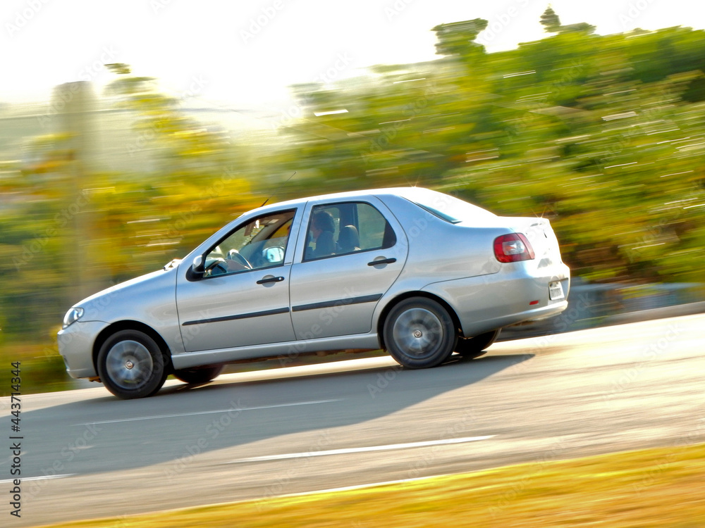 Sylver car moving down the road on sunny day. Blurred nature background