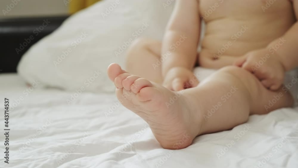 Baby skin care, health care and wellness concept. Unrecognizable baby wearing diaper. Body and legs of one year old toddler sitting on bed. Cute baby feet. Baby skin care, health care and wellness concept. Unrecognizable baby wearing diaper. Body and legs of one year old toddler sitting on bed. Cute baby feet.