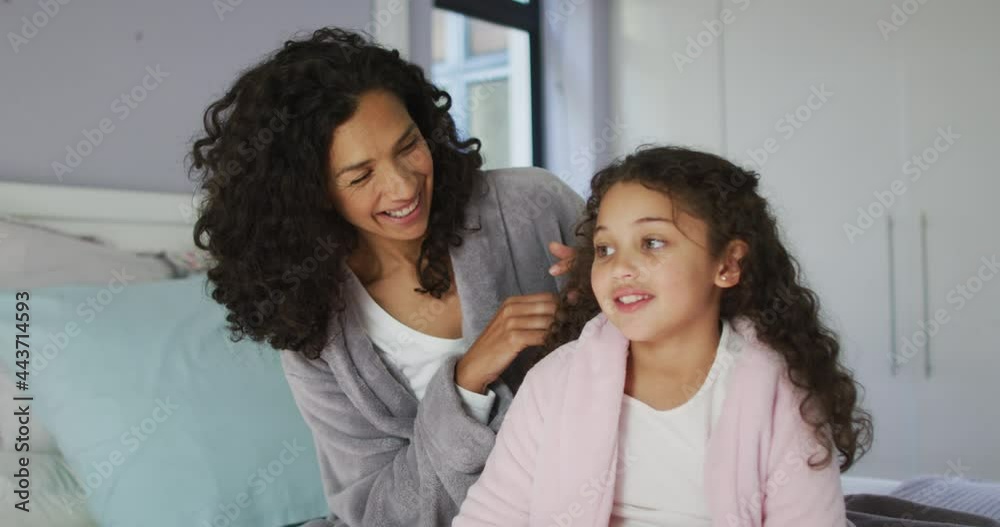 Happy mixed race mother and daughter sitting in bedroom and playing with hairs Happy mixed race mother and daughter sitting in bedroom and playing with hairs