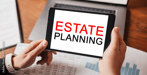 Man hands holding tablet with text Estate Planning at workplace. Businessman working at desk with documents