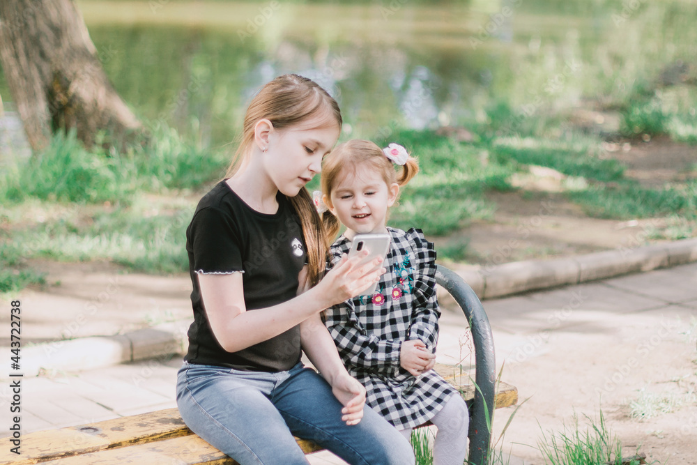 Two sisters sitting on bench in spring summer park and talking in video chat. Two sisters sitting on bench in spring summer park and talking in video chat.