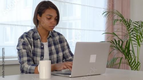 A young woman using a laptop is studying online at home. Cozy office workplace, remote work, e-learning concept