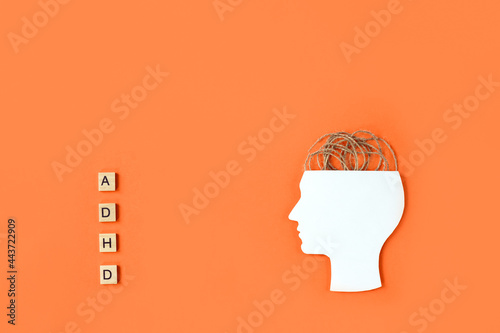 Silhouette of human head, tangled threads and wooden blocks with letters ADHD on orange background. Minimal concept of attention deficit hyperactivity disorder. Copy space photo