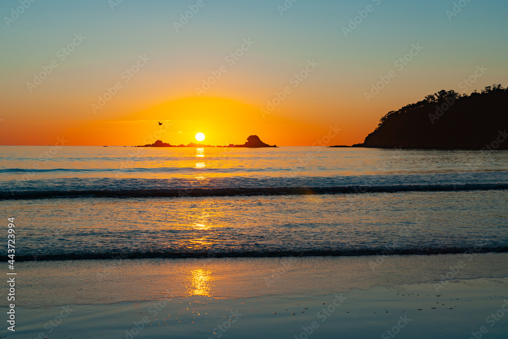 Golden sunrise on horizon with beach, waves and silhouette island.