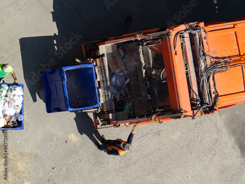 Garbage removal. The scavengers are rolling the trash can to the garbage truck, top view. Garbage loading process. Empty and full trash cans.