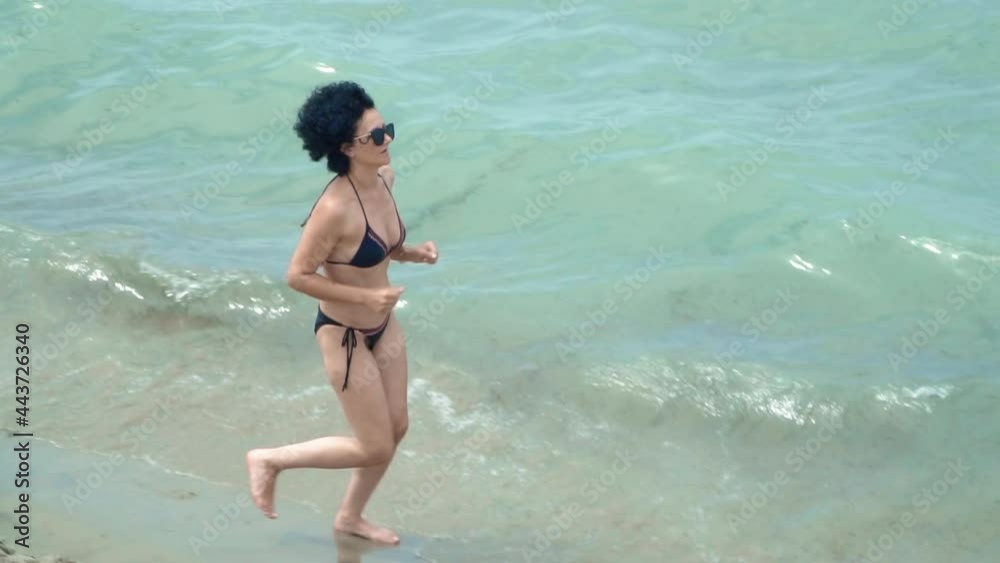 Fit slim woman running, jogging barefoot on seashore wearing bikini, slow motion Fit slim woman running, jogging barefoot on seashore wearing bikini, slow motion