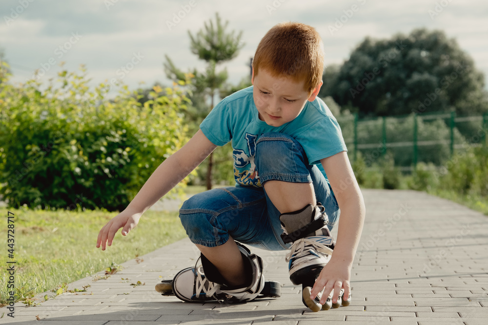 Fototapeta premium A boy tries to get up from the ground after falling with the roller skates. a boy riding a bike or roller, fell and injured his leg