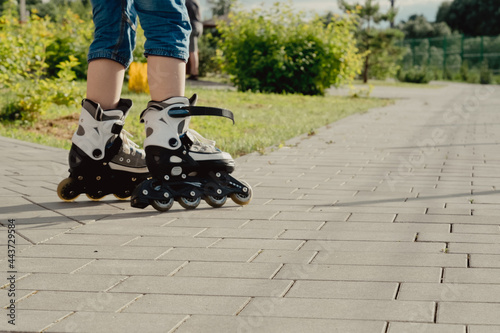 Little boy in protective equipment and rollers stands on walkway in park, low angle view