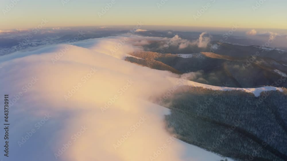 Cloud waves gently and slowly flow over the tops of snow-capped mountains covered with spruce forests at a cold sunset Cloud waves gently and slowly flow over the tops of snow-capped mountains covered with spruce forests at a cold sunset