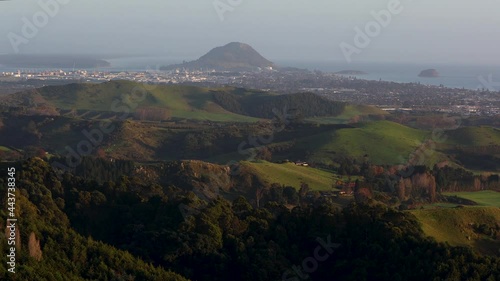 Panning wide reveal shot of Mount Maunganui and main beach at sunrise shot from top of Papamoa Hills. Mount Maunganui, Tauranga, Bay of Plenty, New Zealand photo