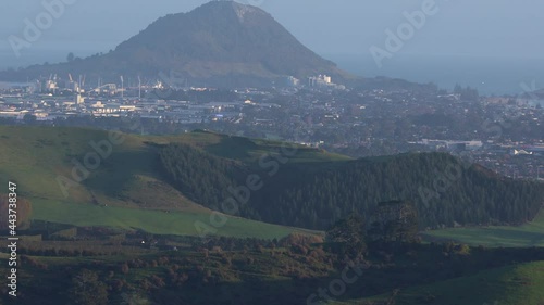 telephoto reveal shot of Mount Maunganui and main beach at sunrise shot from top of Papamoa Hills. Mount Maunganui, Tauranga, Bay of Plenty, New Zealand photo