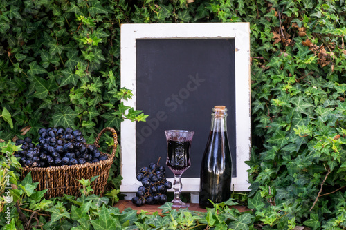 Cup and bottle with wine and basket full with Grapes and Blackboard surrounded by Ivy plant photo