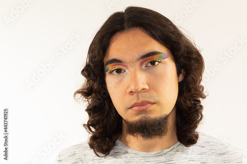 portrait of a gay man made up with a rainbow in his eyes on a white background with a serious face