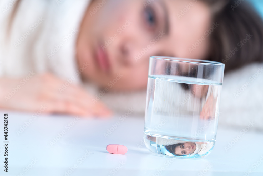 Ill young woman looking at pill and glass of water Ill young woman looking at pill and glass of water