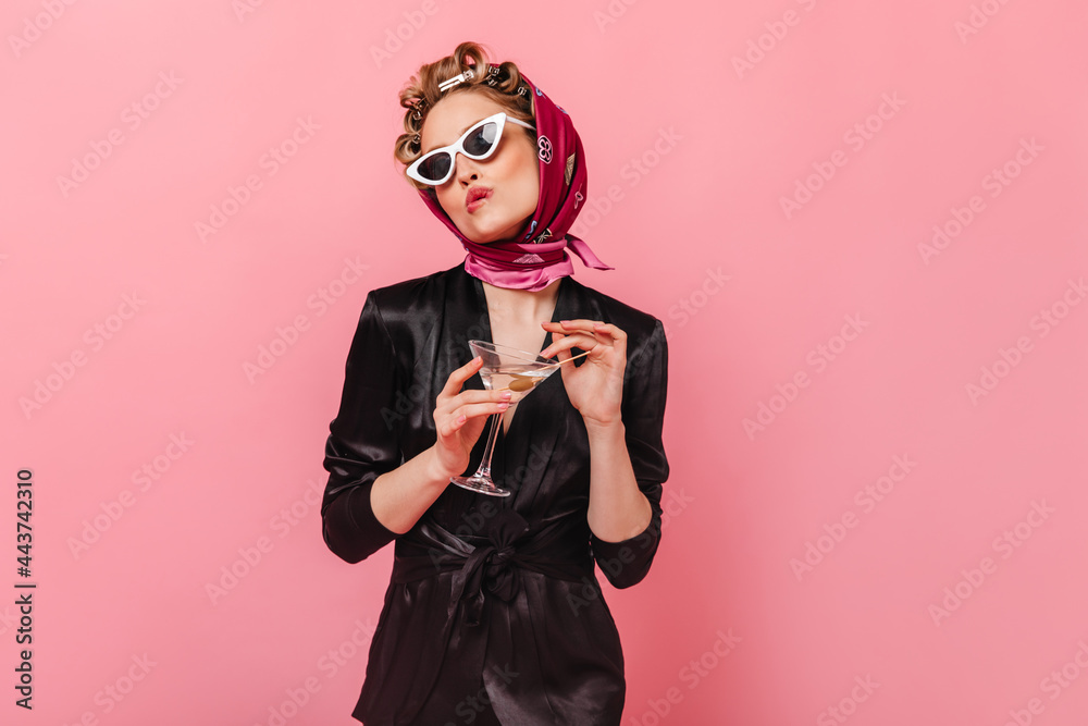 Girl in black dress and scarf bites her lip and poses with martini on pink background Girl in black dress and scarf bites her lip and poses with martini on pink background