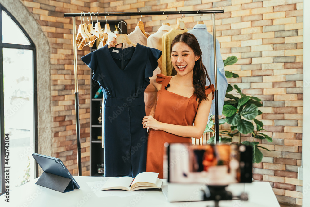 © twinsterphoto - Young and beautiful Asian woman blogger showing clothes in front of smartphone camera while recording vlog video and live streaming at her shop © twinsterphoto - Young and beautiful Asian woman blogger showing clothes in front of smartphone camera while recording vlog video and live streaming at her shop