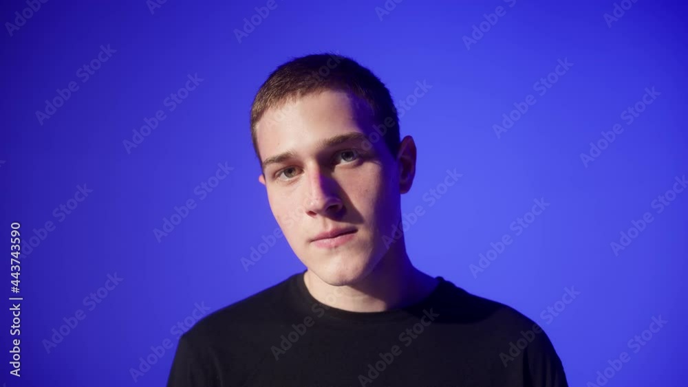 Portrait of talented young man dancer posing on blue neon background in studio. Shooting of modern choreographer. Close-up of male performer in black T-shirt looking in camera. Portrait of talented young man dancer posing on blue neon background in studio. Shooting of modern choreographer. Close-up of male performer in black T-shirt looking in camera.