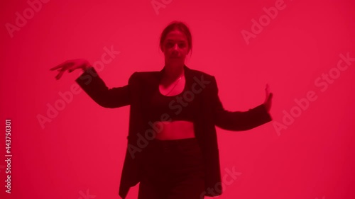 Close-up of woman wearing black jacket dancing vogue on red neon background in studio. Shooting of modern slow dance choreography. Motion of female dancer expressing feelings in dance movings.  photo