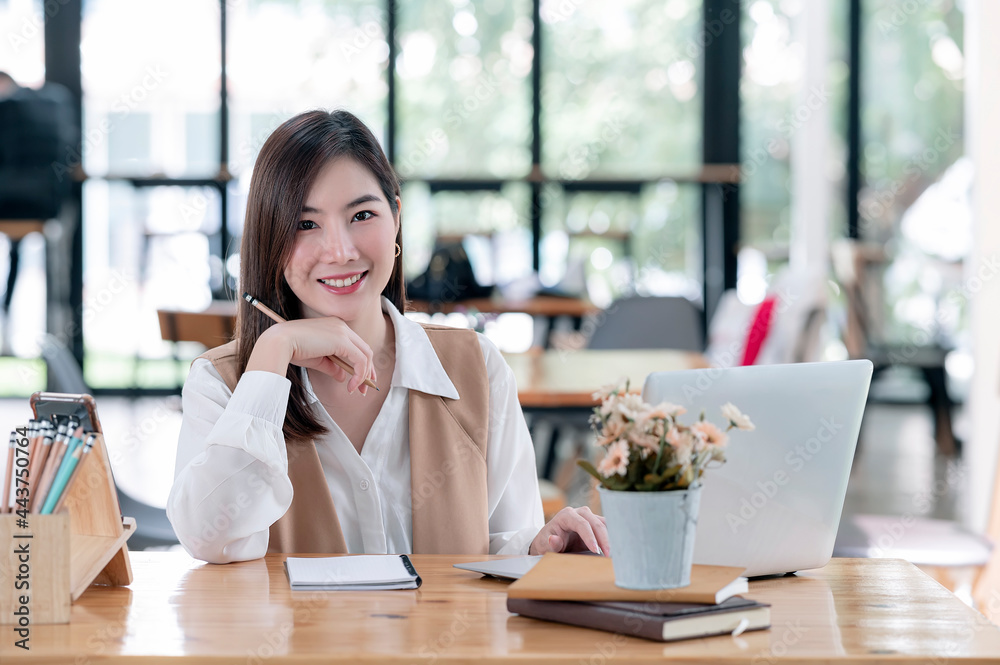 Young beautiful businesswoman smiling and looking at camera while working with laptop at her office desk. Young beautiful businesswoman smiling and looking at camera while working with laptop at her office desk.