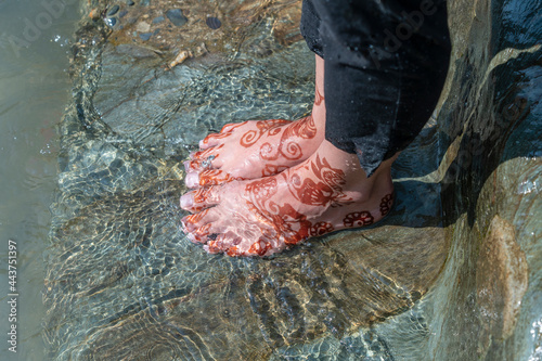 Female feet in the river Ganges water with henna tattoo, close up, India