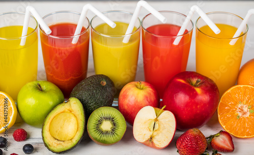 Different fruits juice in glass, apple, orange and strawberry juice with straw, looking refreshing on colourful wood board in front of white wall background. Picture decorating with fresh fruits