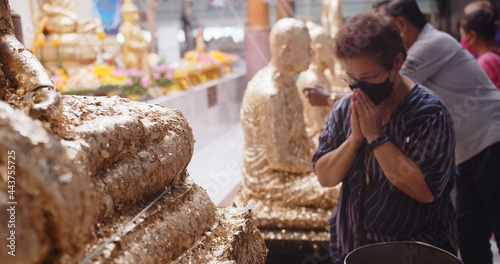 Buddha statue at the temple with soft focus of Asian Buddhist woman praying to the Buddha at Thai temple on holidays with protective face mask covid-19 , Spiritual religious healthcare concept