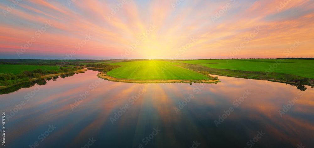 Reflection of a dramatic sunset sky in the calm water of a lake with a green shore