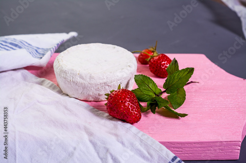 Camembert with strawberries with mint on a pink wooden board on a grey background 