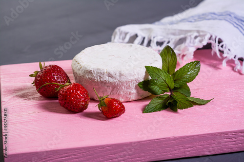 Camembert with strawberries with mint on a pink wooden board on a grey background 