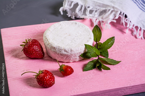 Camembert with strawberries with mint on a pink wooden board on a grey background 