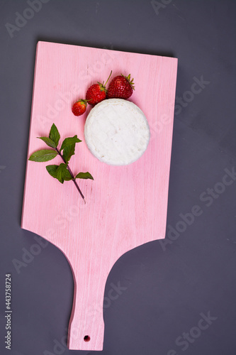 Camembert with strawberries with mint on a pink wooden board on a grey background top